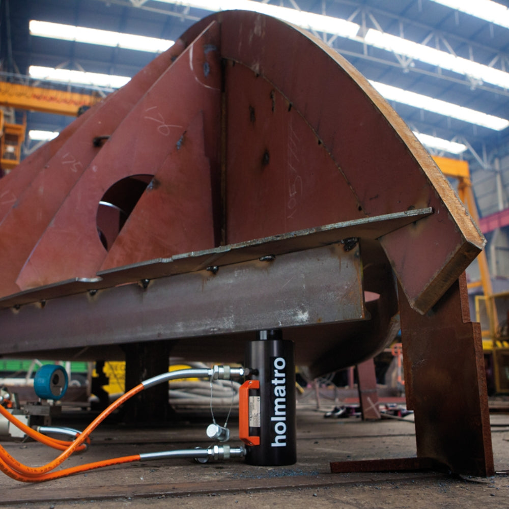 Holmatro donkraft under metalstruktur i industrielt miljø, tilsluttet med orange og sølvfarvede slanger.