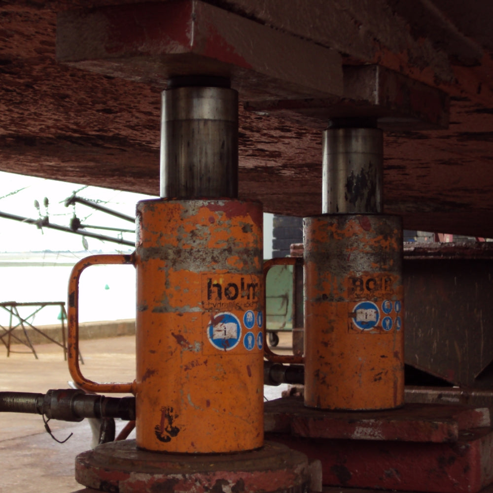 To orange, slidte hydrauliske donkrafte, model "HJ 20/50 G 11", understøtter en tung struktur.