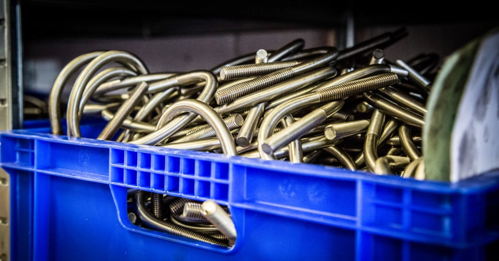 Blå kasse fyldt med U-bøjler med gevindender, stablet i et lagerområde.