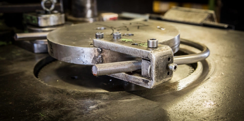 U-bøjle med gevind i begge ender placeret på en rund metalplade i en industriindstilling.