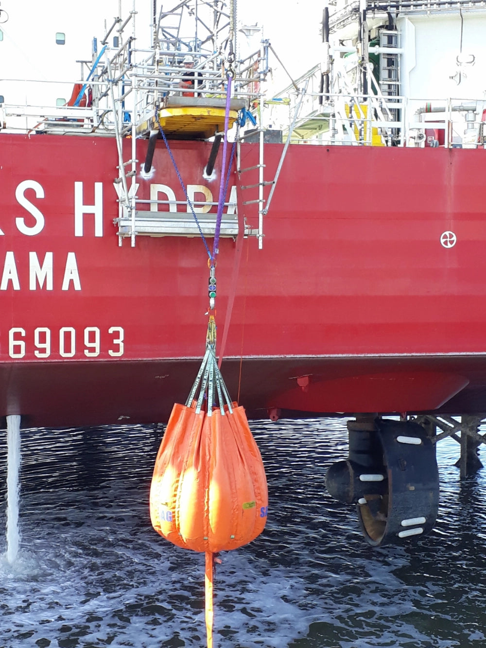 Orange SafetMade Waterbag med "SAFE T BAG" og "2T" tekst, hængende fra skib i maritimt miljø.