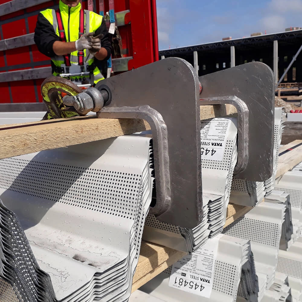 Metalpladegaffel løfter perforerede metalplader, arbejder i baggrunden med sikkerhedsudstyr.
