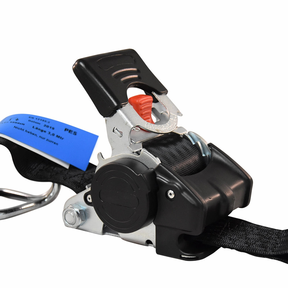 Surringssystem med rød udløserknap, metal kroge, sort rem og blå etiket.